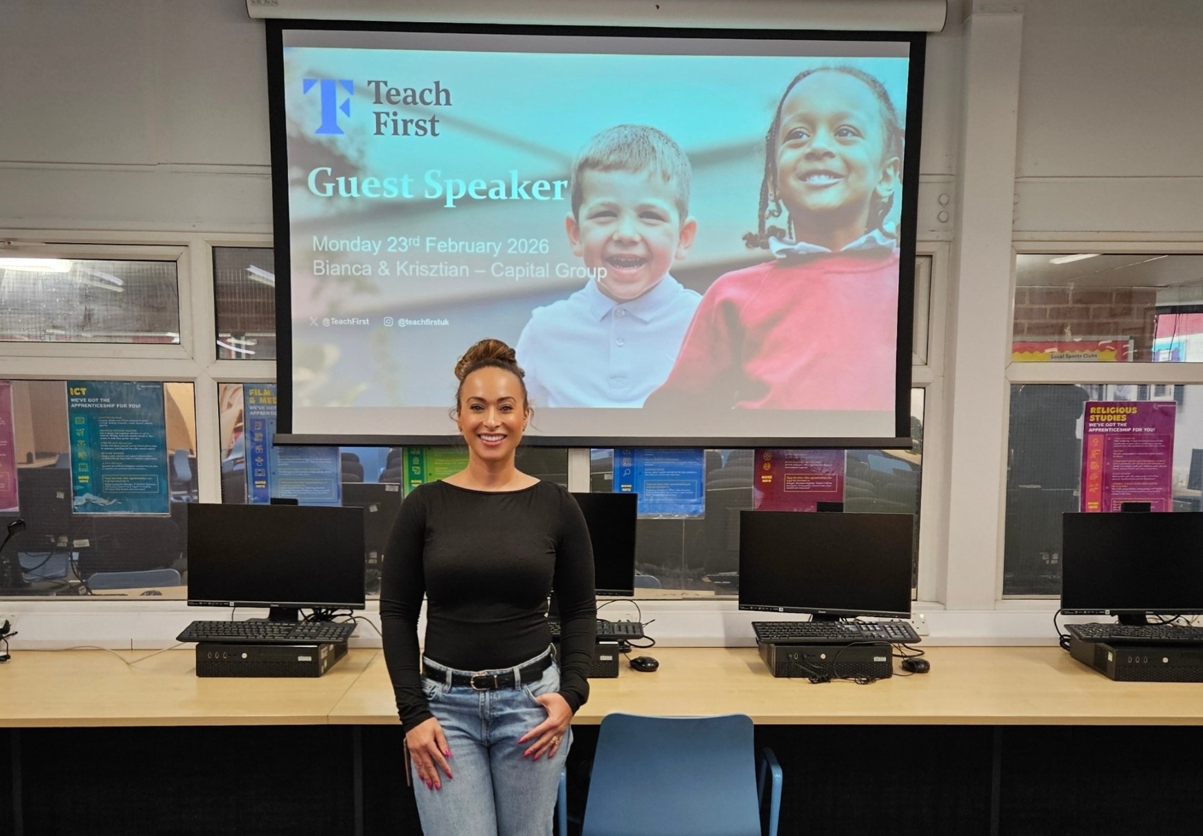 Bianca stands smiling in a school ICT suite in front of a projector screen showing a Teach First ‘Guest Speaker’ slide.