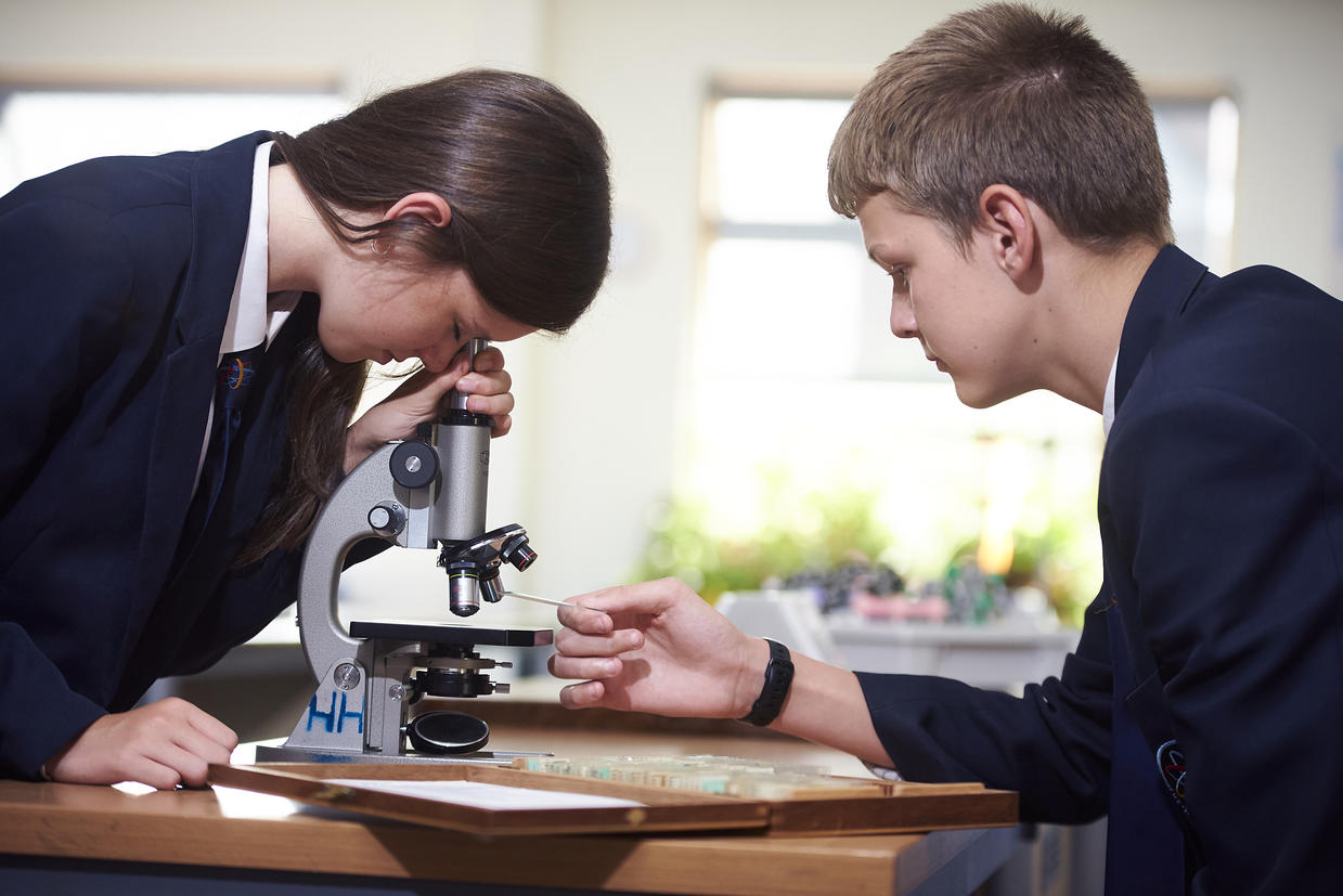 female student looking into microscope near male student holding microscope slide