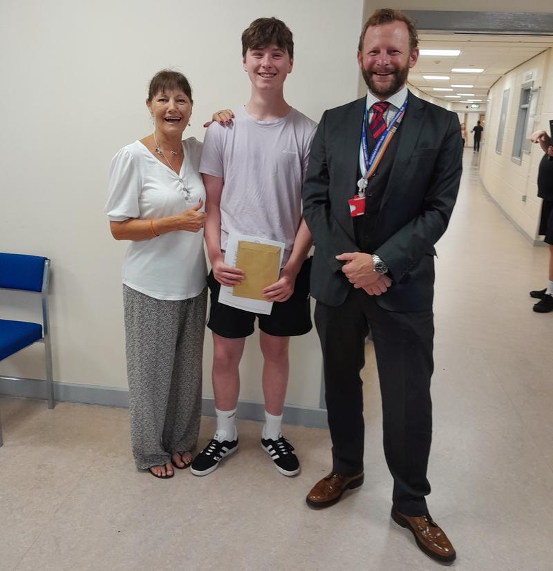 Headteacher standing next to male pupil with their result and their parent