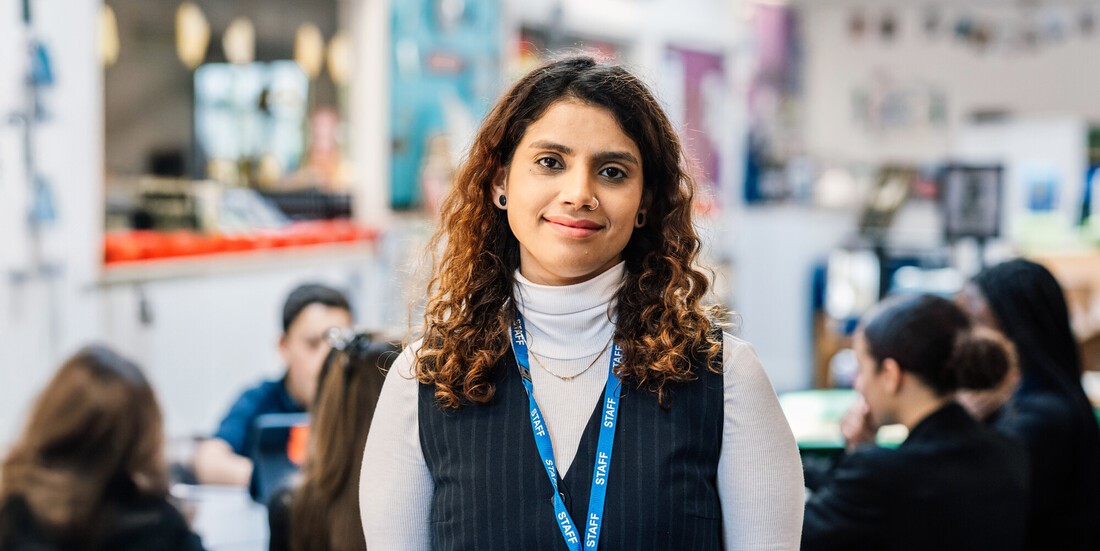 Teacher standing in a classroom with pupils working in the background