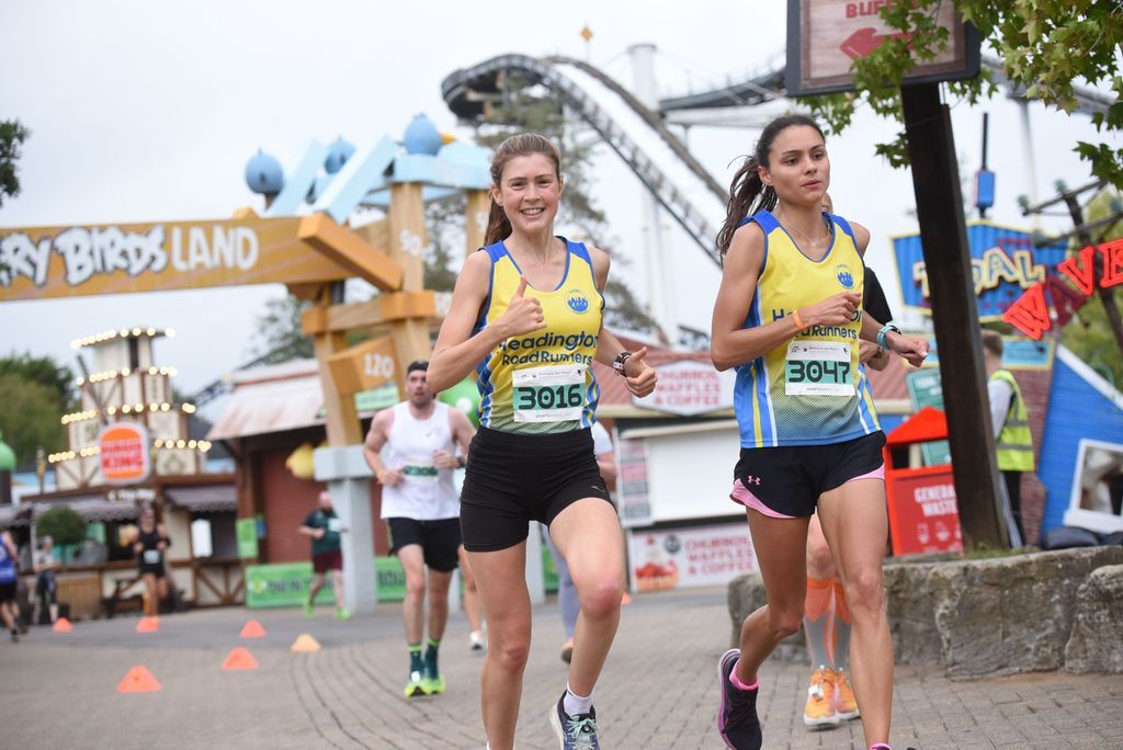 two girls running with a rollercoaster behind her.