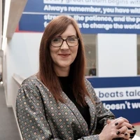 Holly Arles, Teach First ambassador and Principal at City of London Academy Shoreditch Park, smiling while seated in a modern office space with motivational Teach First quotes in the background.