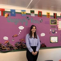 Hetta standing in front of a colourful ‘Geography Rocks’ classroom display.