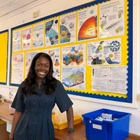 Keziah smiling in a classroom in front of a display board filled with science posters.
