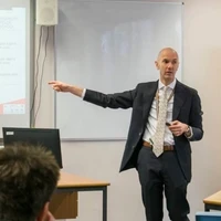 Tim Fox, a teacher, presenting to students in a classroom with a slide projected behind him.