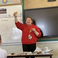 A teacher holding up pupil work in front of a whiteboard during a classroom lesson.