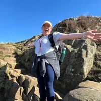 Fran smiling with her arms outstretched while walking on a rocky hillside under a bright blue sky.
