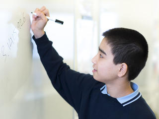 young male student writing out pi on a whiteboard