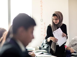 teacher walking in between tables in a classroom smiling