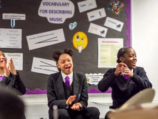 three students sitting in a classroom smiling and clapping