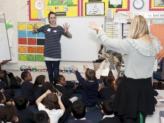Two teachers in a classroom interacting with children seating on the floor