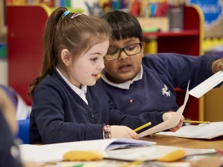 two primary school children help each other with work