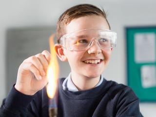 Child in protective goggles smiling in front of a Bunsen burner