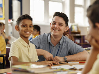 Teacher and student sat at table and smiling at camera