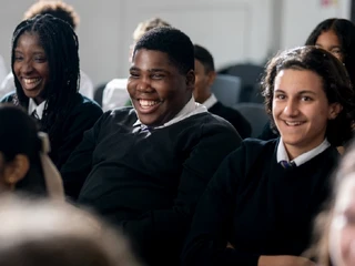 Smiling secondary school students in uniform sitting together and enjoying a classroom activity.