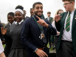 A teacher celebrating with a group of smiling secondary school pupils in school uniform.