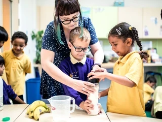 A teacher helping primary school pupils with a science experiment in a classroom.