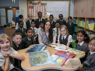 Pupils sitting with a teacher around a table of books in a school library.