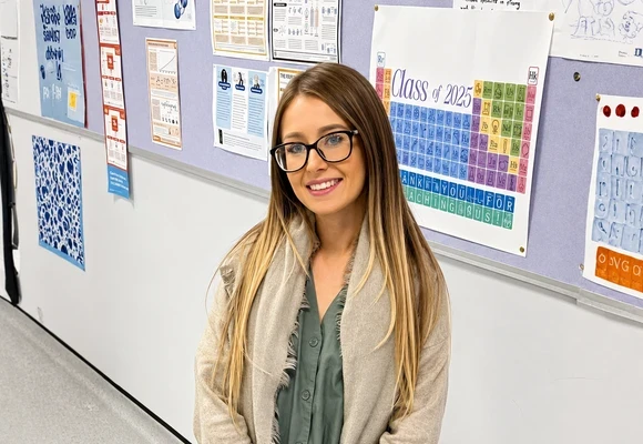 Devon standing in a school corridor in front of classroom displays and science posters.