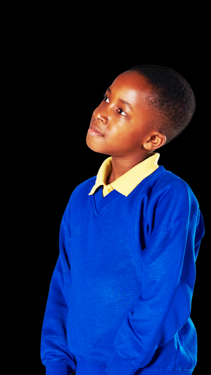 Boy in blue primary school jumper stands in front of black background