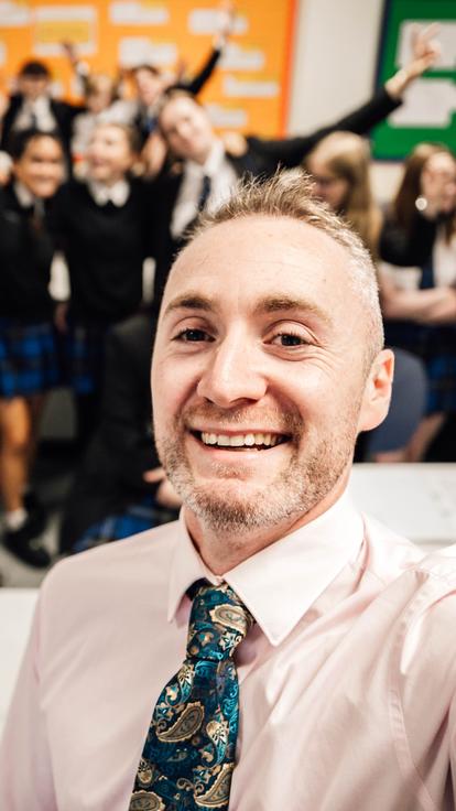 Teacher taking a selfie while school children smile in background