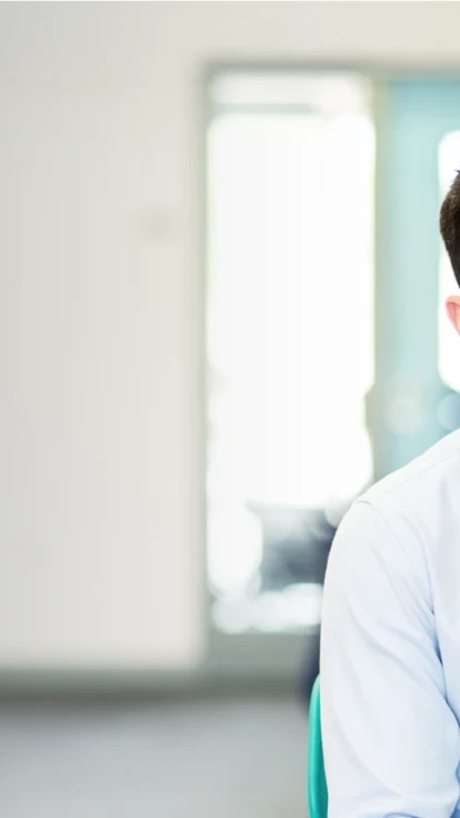 Smiling male coachee in a shirt and tie sitting at a desk in a modern classroom.