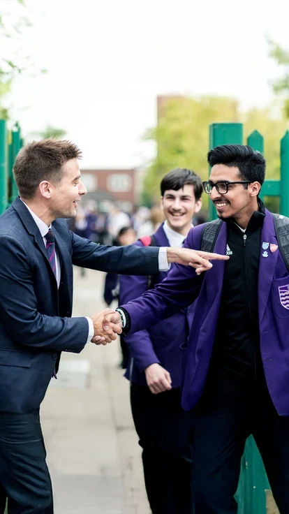 Teacher greeting pupils at school gate.