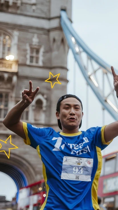 Runner wearing a Teach First shirt celebrating near Tower Bridge during Run the River.