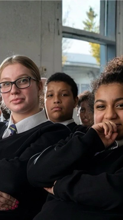 A group of secondary school pupils in school uniform sitting together in a classroom, looking towards the camera.