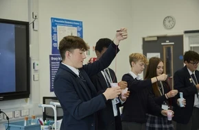 Secondary school students in a science classroom carrying out an experiment using liquids in cups.
