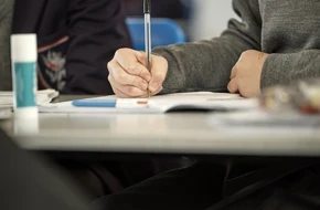 Pupil writing in a notebook during class, focused and supported in their learning environment.