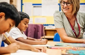 Teacher smiling as primary school pupils write in their books during a classroom lesson.