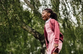 Young pupil enjoying outdoor learning in a woodland setting, smiling and engaged in nature.