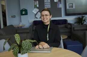 Teacher sitting at a table with a laptop in a school staffroom.
