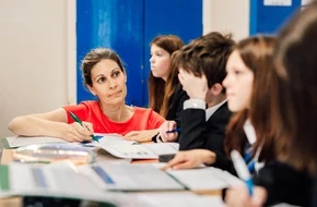Teacher supporting secondary school pupils as they work on written tasks in a classroom.