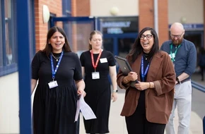 Four education professionals wearing lanyards walking and talking outside a school building.