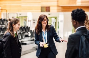 Teacher speaking with two secondary school pupils in a school hall.
