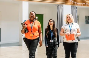 Three teachers wearing lanyards walking together and talking outside a school building.