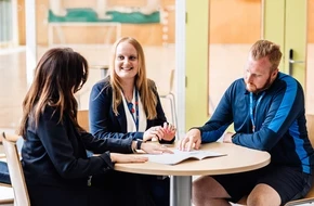 Three teachers sitting around a table discussing documents during a meeting in a school.
