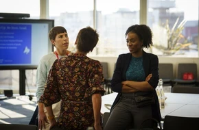 Three professionals talking together during a meeting in a conference room.