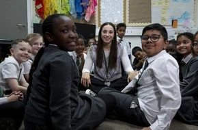 Teacher sitting with a group of pupils in a classroom during a group discussion.