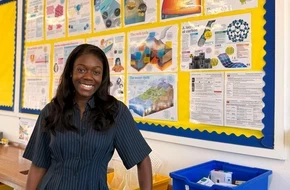 Keziah smiling in a classroom in front of a display board filled with science posters.
