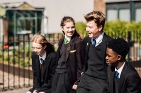 Four secondary school pupils in uniform walking together outside their school and talking.