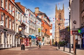 Street scene in Derby city centre with historic buildings, shops and Derby Cathedral in the background.