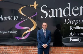 Stuart standing outside Sanders Draper School in front of the school's sign.