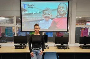Bianca stands smiling in a school ICT suite in front of a projector screen showing a Teach First 'Guest Speaker' slide.