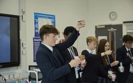 Secondary school students in a science classroom carrying out an experiment using liquids in cups.